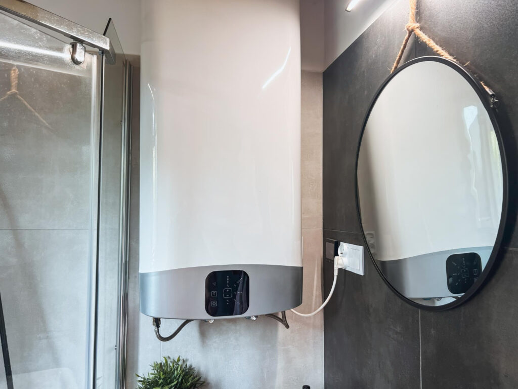 Is Your Sidney Water Heater Leaking? Here's What to Do 7 Tankless water heater mounted on wall in modern bathroom setting with mirror and electrical outlet, relevant to home HVAC solutions and maintenance tips for homeowners.